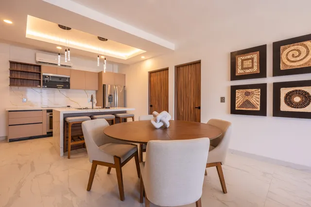 Comedor con obras de arte y cocina abierta en el departamento modelo de Vista Los Sueños