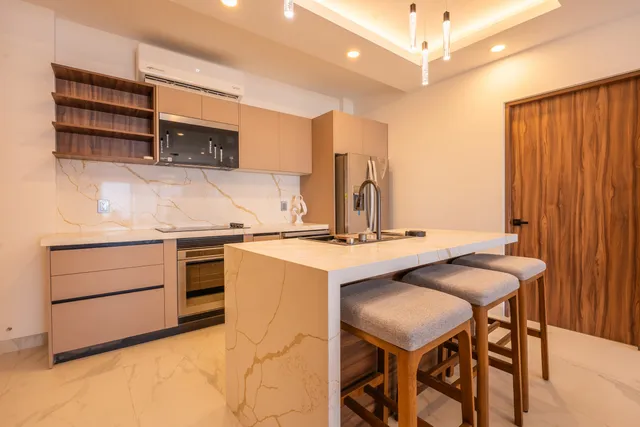 Cocina con isla de mármol, bancos de barra y electrodomésticos de acero inoxidable